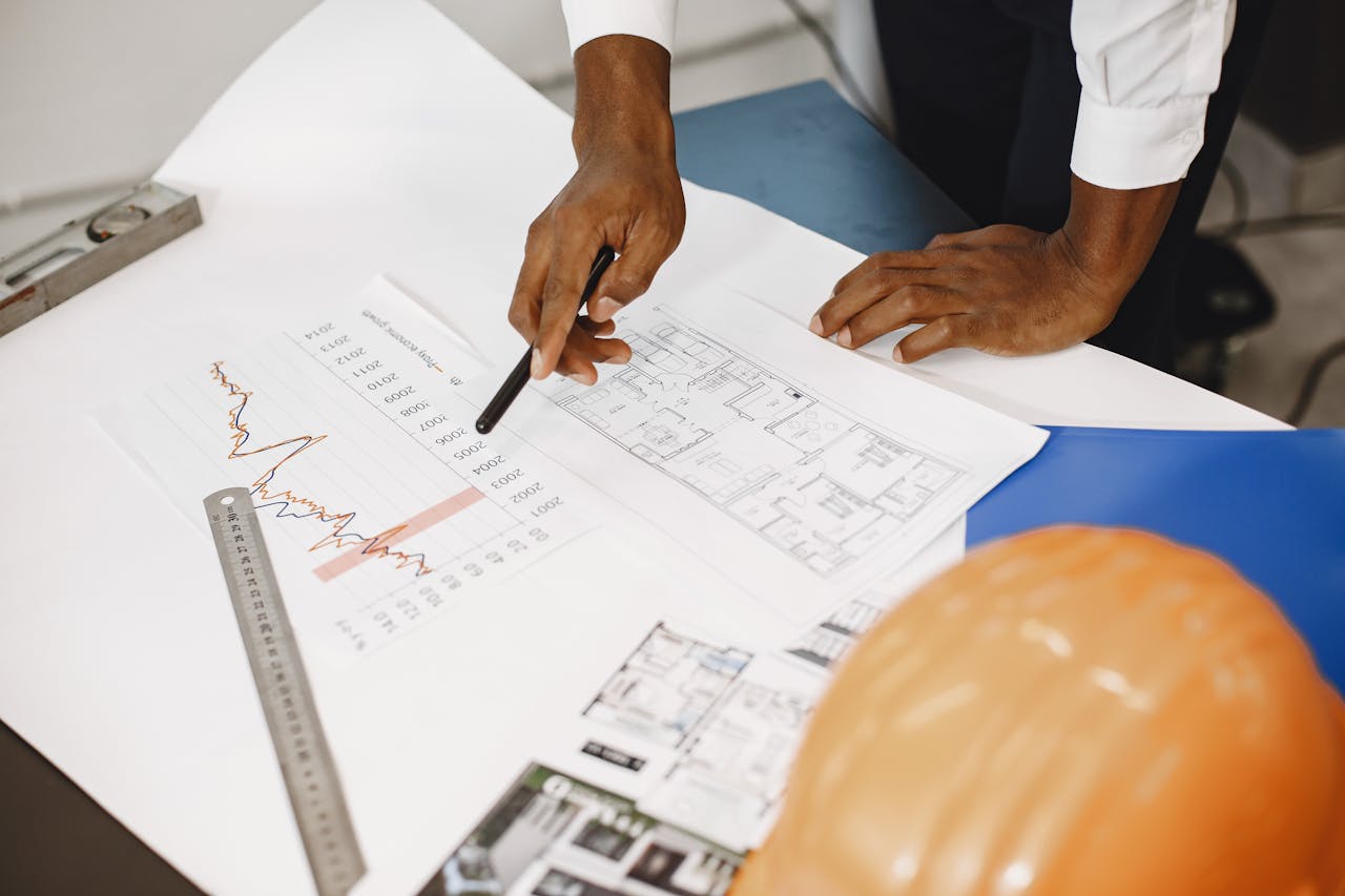 portfolio-01 Hands of an architect analyzing blueprints and financial graphs at a desk.