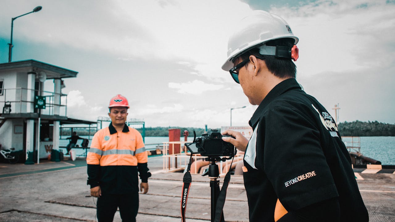 The Art of Drawing Readers In: Your attractive post title goes here Two construction workers in safety gear filming at a waterfront location.